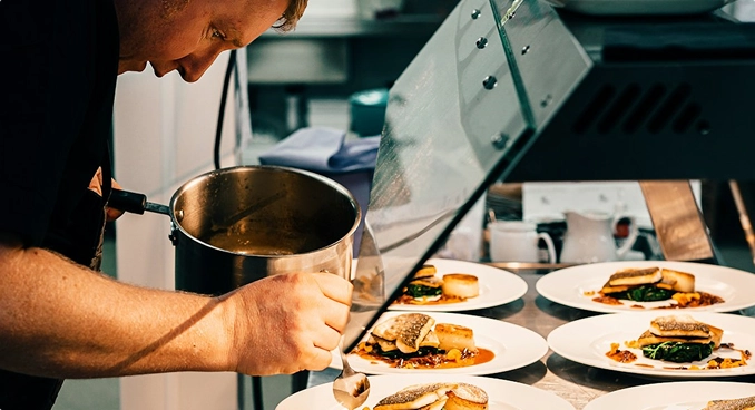 A chef carefully finishing several plated dishes in a professional kitchen.