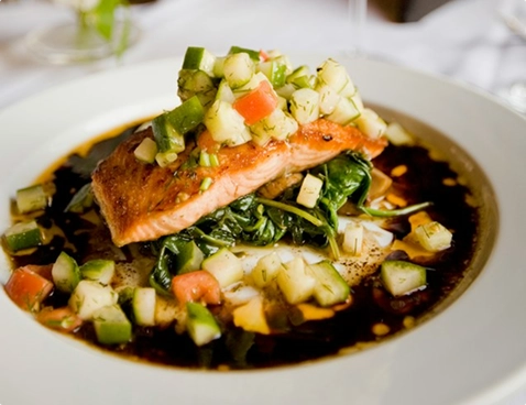 A grilled salmon fillet served with colourful seasonal vegetables and sauce.