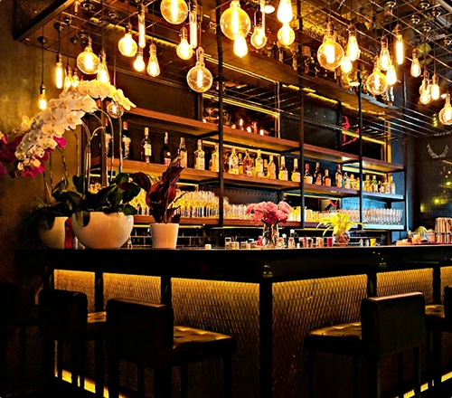 An elegant bar with high stools, dark finishes and numerous warm hanging lights.